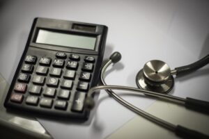 A calculator and a stethoscope alongside each other on a grey table. 