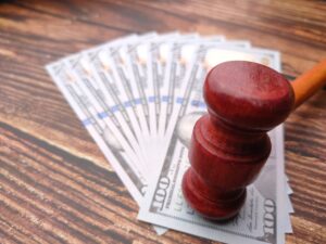 A few money notes spread out in a fan with a red gavel on top on an oak table to represent medical negligence compensation.