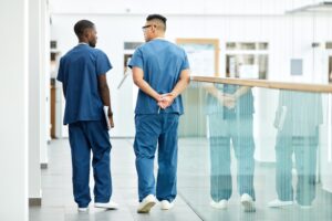 Two doctors wearing blue uniform having a chat walking down a hospital corridor. 