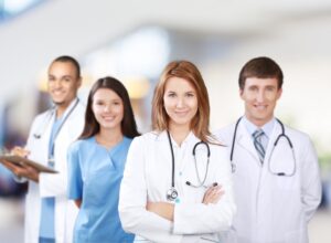 Four medical professionals wearing their uniform stood in a row together smiling. 