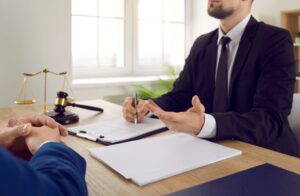 A medical professional solicitor sat on a desk talking to a client with paperwork and a gavel in front of him. 