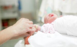 A newborn baby wrapped in a white blanket, with someone holding their hand.