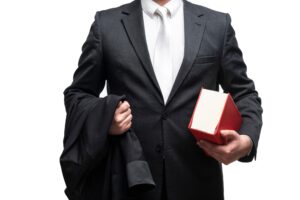 A torso shot of a solicitor in a suit carrying his suit jacket and a red law book.